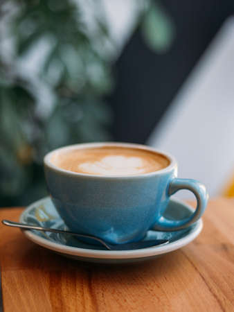 One Cup of cappuccino with latte art. Coffee in blue cup on wooden table in cafe. Concept of easy breakfast.の写真素材