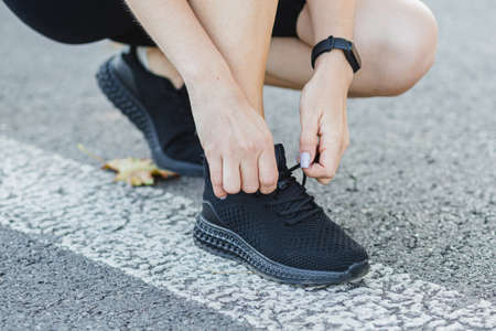 Fitness woman tying shoelaces outdoors. Tie sneakers. Sport and healthy active lifestyle concept. Girl lacing up sport shoes before training sessionの写真素材