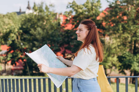 Attractive young female tourist is exploring new city. Unhappy redhead Woman with map in hands lost...