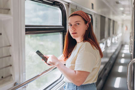 A beautiful hipster woman with smartphone travelling on the train in Europe. Tourist travel, surf...
