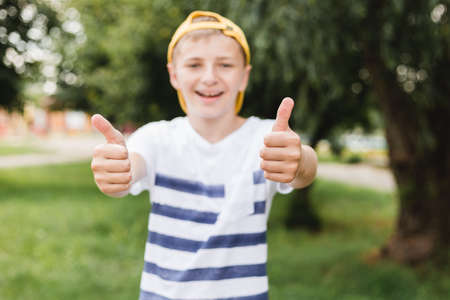 Teenage smile boy showing thumb up gesture on nature background, gesture concept. Boy wearing on stripe t-shirt and yellow hatの写真素材