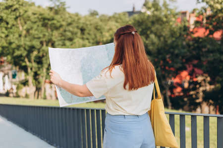Attractive young female tourist is exploring new city. Happy redhead Woman with map in hands