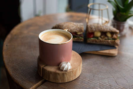 One Cup of cappuccino with latte art. Coffee in pink cup and sandwich with ham, cheese, bacon, tomatoes in cafe. Concept of easy breakfast. Rustic styleの写真素材