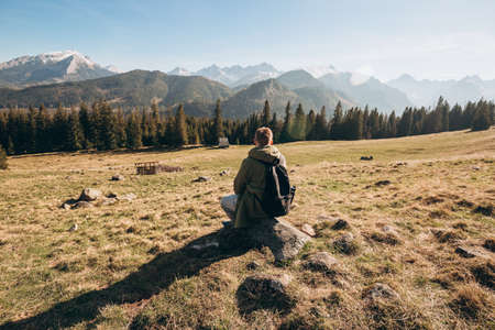 Young man in sunglasses with backpack see view on top mountain. Freedom, happiness, travel and vacations concept, outdoor activities. Man standing backwards looking awayの写真素材