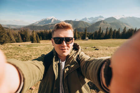 Young man in sunglasses making selfie photo high in the snow mountains enjoying the view. Freedom,...
