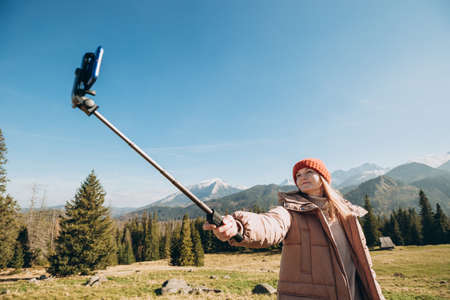 Young woman making selfie photo high in the snow mountains enjoying the view. Freedom, happiness, travel and vacations concept, outdoor activitiesの写真素材