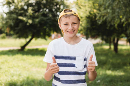 Teenage smile boy showing thumb up gesture on nature background, gesture concept. Boy wearing on stripe t-shirt and yellow hatの写真素材