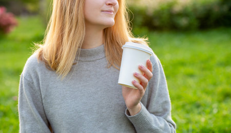Close up portrait of an attractive young blonde woman drinking coffee at summer park. Food, rest,...