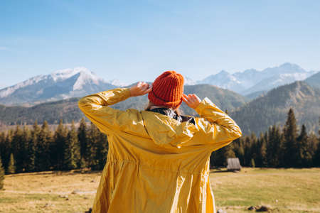 Happy blonde Woman in red hat standing backwards looking away. Traveling in the mountains. Freedom, happiness, travel and vacations concept, outdoor activities.の写真素材