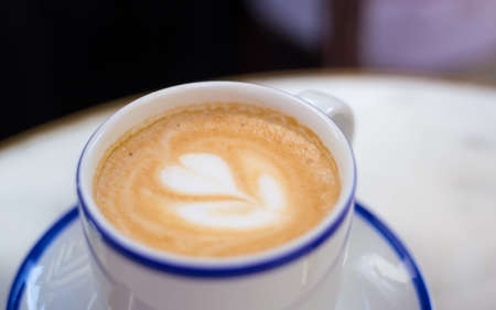 One Cup of cappuccino with latte art. Coffee in blue cup on wooden table in cafe. Concept of easy...