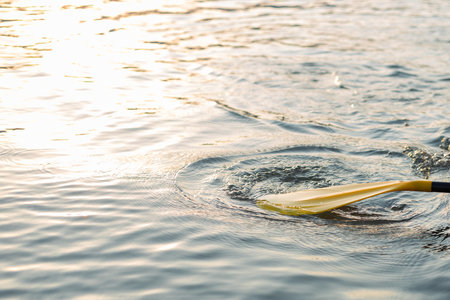 Yellow Paddle board on blue clean water surface background. Surfing and SUP boarding equipment in...