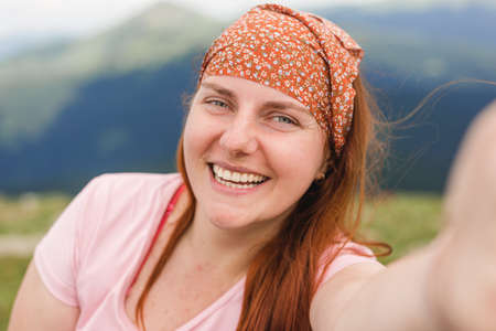 Lovely woman making selfie against the background of the mountain valley. Traveling in the mountains. Freedom, travel banner. Online communication conceptの写真素材
