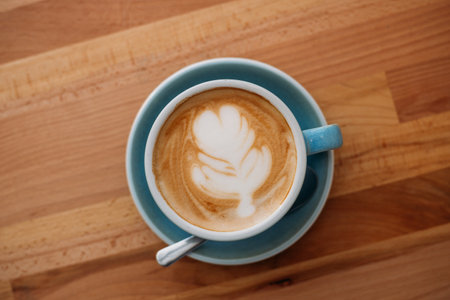 Cup of cappuccino with latte art. Coffee in a blue cup on a wooden table in a cafe. Concept of easy breakfast. Top view, big mugの写真素材
