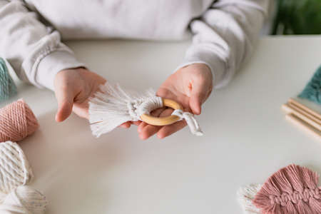 Hand of a woman when she is making macrame. Natural cotton threads and wooden beads. Handmade macrame belt in work process. Female hobby.の写真素材