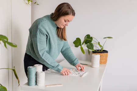 Woman making a macrame work inside her house. Natural cotton threads and wooden beads. Handmade...