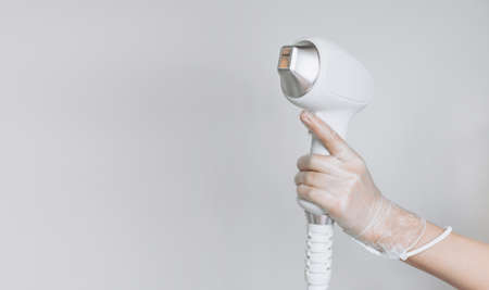 Laser device for removing unwanted hair in the hand of nurse. Laser hair removal, cosmetic body treatments. Concept of hygiene, beauty, health. Girl holding a working part of the epilator in her handの写真素材