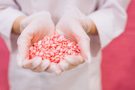 Wax for depilation of pink color in the form of a heart. The concept of depilation, waxing, smooth skin. Copy space, banner, flyer. Hard wax beans in woman palmsの写真素材