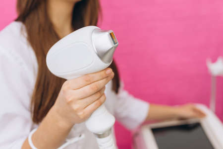Laser device for removing unwanted hair in the hand of nurse. Laser hair removal, cosmetic body treatments. Concept of beauty. Girl holding a working part of the epilator in hands on pink backgroundの写真素材