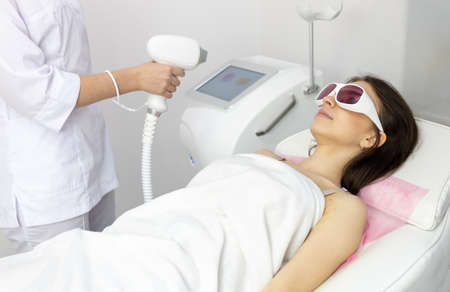 A woman tunes a laser hair removal machine. Girl holding a working part of the epilator in a modern beauty salon. Hair removal, laser procedure at medical clinic, spa concept. Laser skin care bannerの写真素材