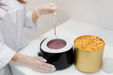 Violet hot liquid wax for depilation on a wooden stick. The concept of depilation, beauty, skin...