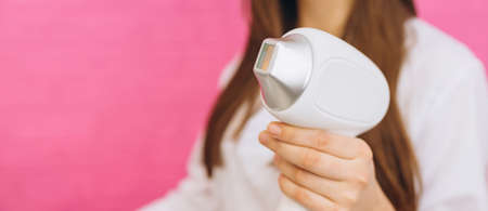 Laser device for removing unwanted hair in the hand of nurse. Laser hair removal, cosmetic body treatments. Concept of beauty. Girl holding a working part of the epilator in hands on pink backgroundの写真素材