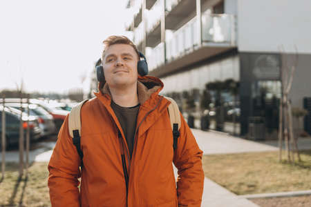 A handsome young man listening to music with headphones and standing on the street in the city....