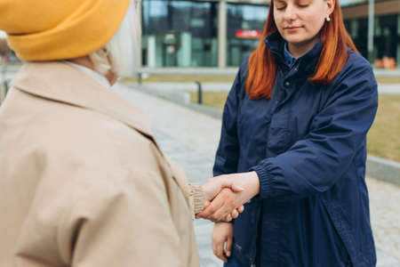 Two women friends or female partners meet on sity street. Successful business. Handshake of two business women on the background of modern buildings, partnership concept, Shaking hands to seal a dealの写真素材