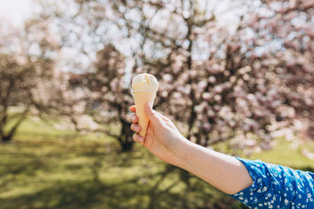 Close up womans hand with delicious white ice cream in waffle cone outdoors. Spring time, food...