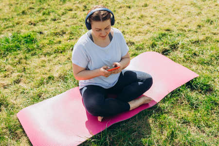 Beautiful young redhead woman relaxing with Smartphone on Yoga Mat after Training. Happy girl with...