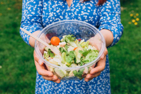 Hand of woman holding bowl with salad over isolated nature background. Healthy picnic, food banner
