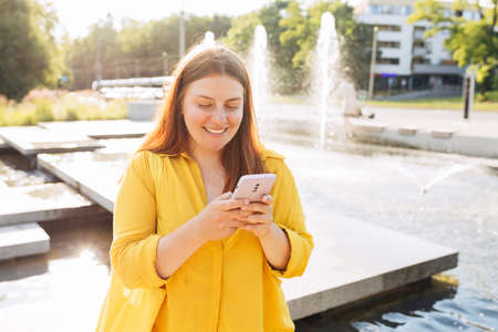 Beautiful stylish woman walking in the city on summer day and holding smart phone. Phone...
