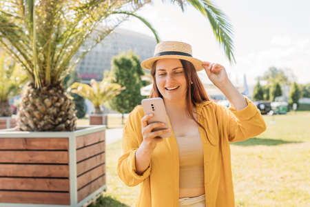 Pretty laughing girl with smartphone has a good time in summer weekend. Trendy lady with brown hair...