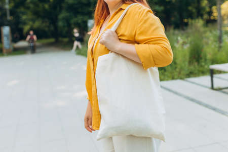 Woman with white cotton shopping bag in her hands in the city street. Mockup and zero waste concept....