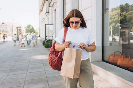 Beautiful fashionable young woman in sunglasses with shopping paper bag standing on city street, black friday. Urban lifestyle concept. Delivery carrying.の写真素材