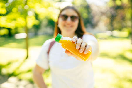 Young stylish happy woman with juice standing over nature background. Redhead girl walking in the...