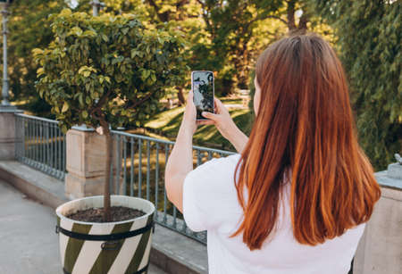 Young woman using smartphone outdoor capture picture of tree. Mobile phone in a womans hand. Beautiful young girl is smiling while taking photo of nature background, Urban lifestyle concept.の写真素材