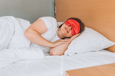 Young beautiful woman sleeping in bed with pink eye mask. Millennial Caucasian girl sleeping on soft pillow, enjoying sweet dreams good night rest in bed.の写真素材