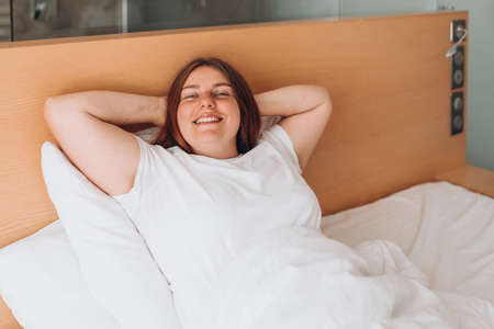 Portrait pretty young girl on bed in modern apartment in the morning. Enjoying the morning, beautiful woman resting in the room at homeの写真素材
