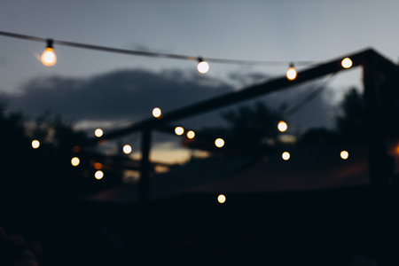 Decorative outdoor string lights at night time, Defocused Background, night city life backdrop, party time with Yellow bokeh ballsの写真素材