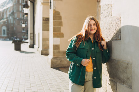 Young happy woman traveler with a backpack traveling Europe in autumn. Stylish female foreigner examines architectural monument during her long-awaited vacationの写真素材