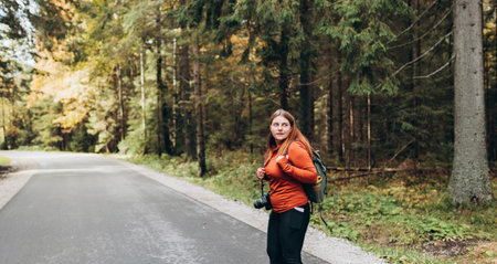 Stylish Tourist Woman hiking on footpath in autumn forest. Happy redhead person in active trekking clothes walking on nature backgraund. Travel and active lifestyle concept.の写真素材