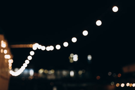 Decorative outdoor string lights at night time, Defocused Background, night city life backdrop, party time with Yellow bokeh ballsの写真素材