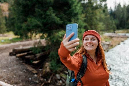 Woman in red hat uses a telephone for take pictures, makes selfies and video calls family from home on mountains background. Travel and wanderlust concept. Amazing chill momentの写真素材