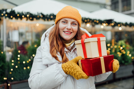 Happy young beautiful excited woman holding gift boxes in hands and smile on winter street. Winter holidays sale. Concept of shopping, holidays and happiness christmas.の写真素材