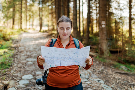 Stylish woman holding paper map relaxing in nature. Travel and active lifestyle concept. Hiking...