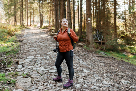 Solo tourist Woman hiking on footpath in autumn forest. Full body photo. Happy redhead person in active trekking clothes walking on nature backgraund. Travel and active lifestyle concept.の写真素材