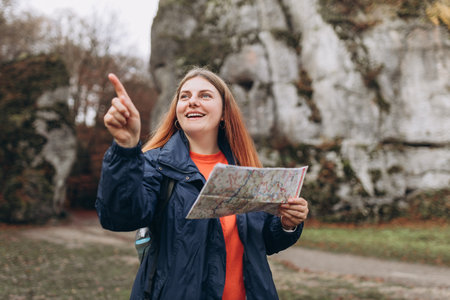 Happy redhead Woman with map hiking in woods. Adventure women pointing finger on mountains background. Freedom and active lifestyle concept. Amazing chill momentの写真素材