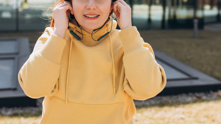 Young woman listening to music via headphones on the street. Pretty happy redhead woman standing on urban background and holding the headphones, spring dayの写真素材