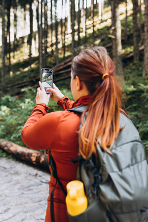 Happy Woman uses a telephone for take pictures on forest background. Travel and wanderlust concept. Amazing chill momentの写真素材