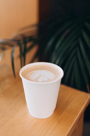 White Paper cup of coffee with latte art on wooden table. Street coffee, top view. Cup coffee in...